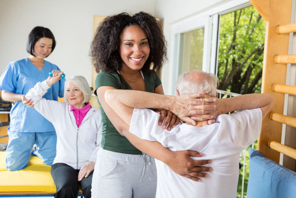 Smiling caregivers helping older adults with their stretching