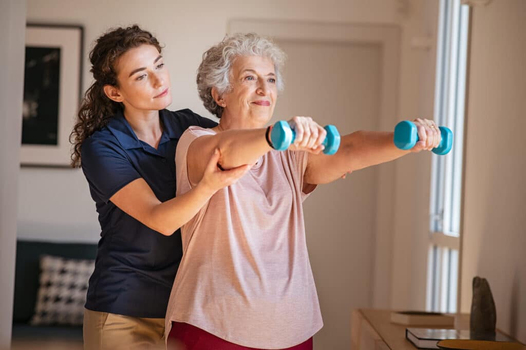 A female caregiver helping an older woman raise dumbbells